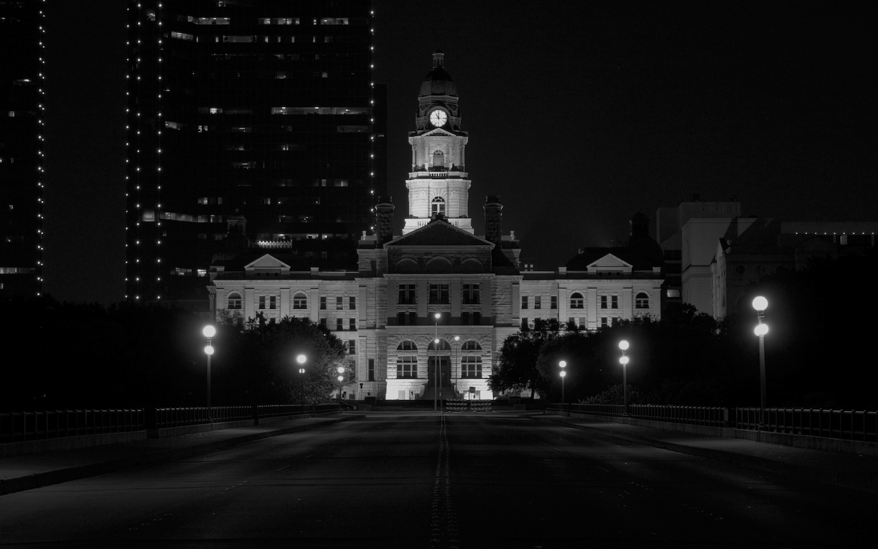 Historic clock tower at night with modern high-rise buildings in the background. Fort Worth's Court House.