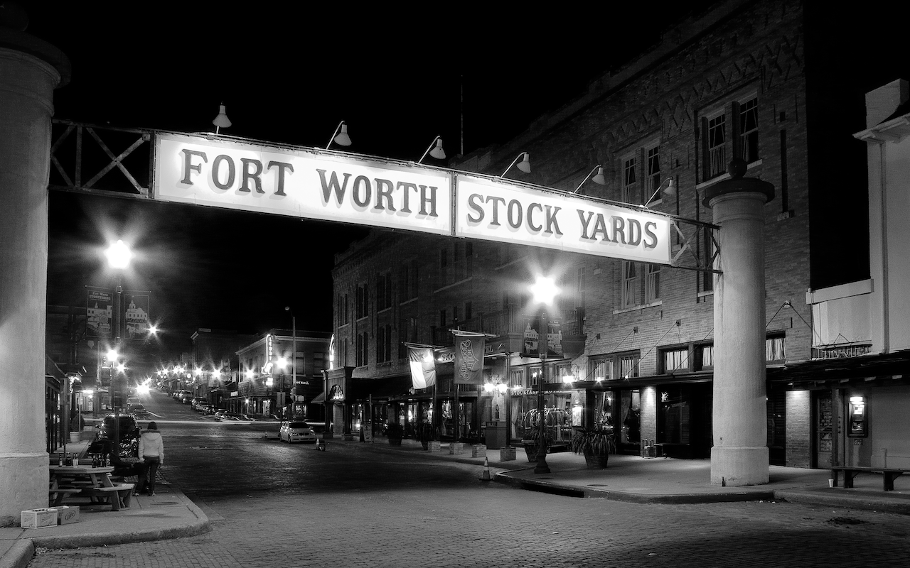 Black and white photo of Fort Worth Stock Yards sign at night.